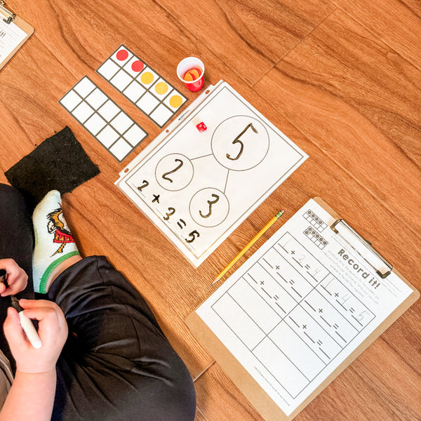 Child sitting on the floor with educational materials including a whiteboard with numbers and a pencil.